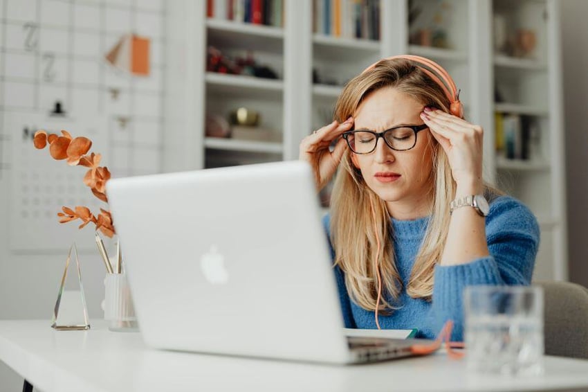 Woman sitting in front of laptop with eyes shut massaging her temple