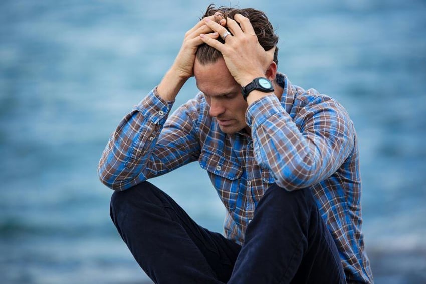 Man in blue shirt looking down and pulling his hair