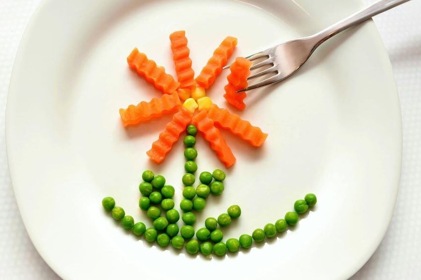 Plate with cut up carrots, corn and peas in the shape of a flower