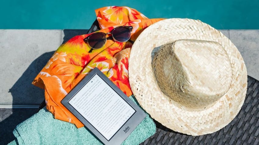 Hat, sunglasses and e-reader resting on towel by a pool
