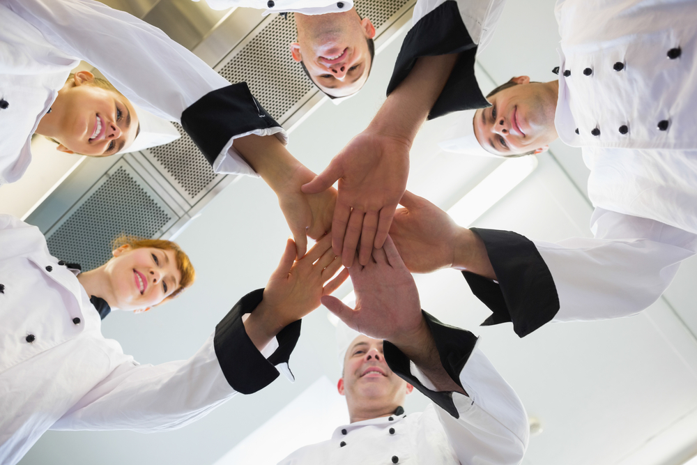 Restaurant kitchen crew joining hands in a team huddle